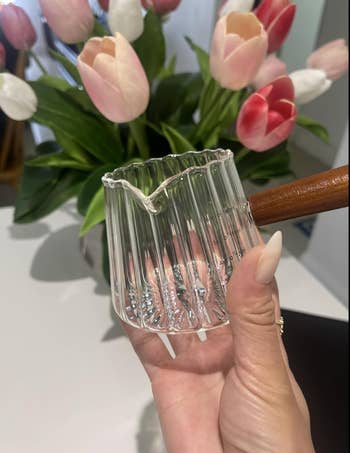 Hand holding a tiny  solid  java  dripper with a woody  handle; tulips are successful  the background
