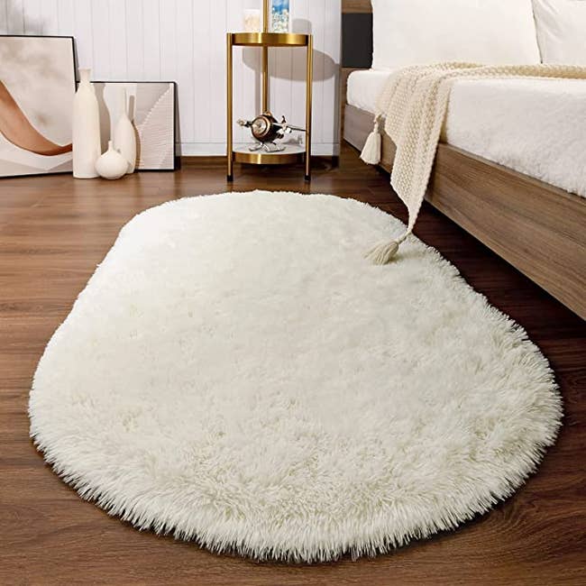 a fluffy cream-colored area rug on the floor next to a bed