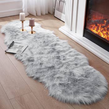 Faux fur rug in a cozy living room by a fireplace, with two candles on golden holders and an open magazine nearby