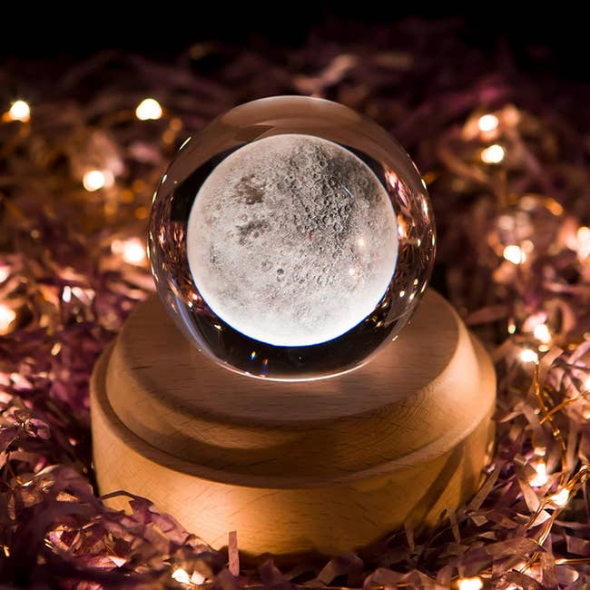 Glass moon sphere on a wooden stand surrounded by decorative lights