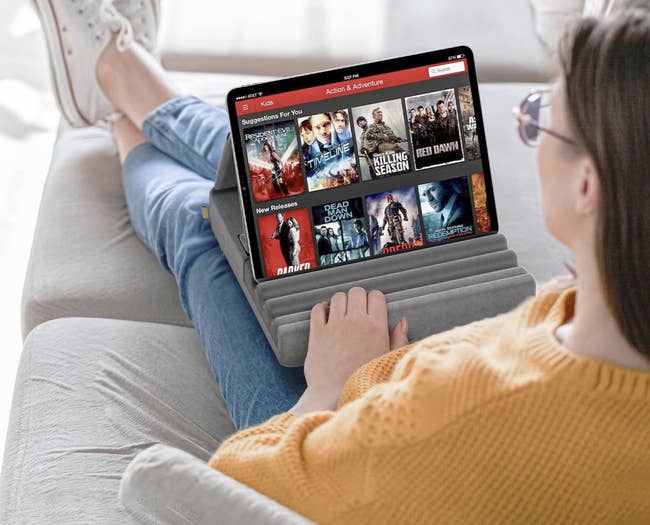 Person relaxing connected a couch, watching enactment and escapade movies connected a tablet. Display shows movie suggestions and caller releases