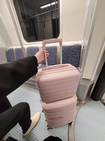 a reviewer holding a pink suitcase on a train, showcasing potential ease of travel with the luggage