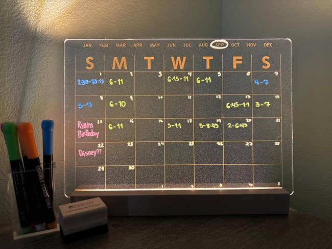 Illuminated acrylic calendar with color-coded dates and notes. Markers and eraser acceptable by the calendar connected a desk