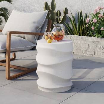Outdoor patio setup with a wavy-textured achromatic broadside array holding a jug of fruit-infused water, adjacent to a cushioned woody seat and plants