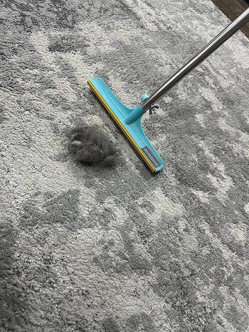 Reviewer's Uproot hair cleaner broom next to a gigantic ball of hair it removed from reviewer's carpet