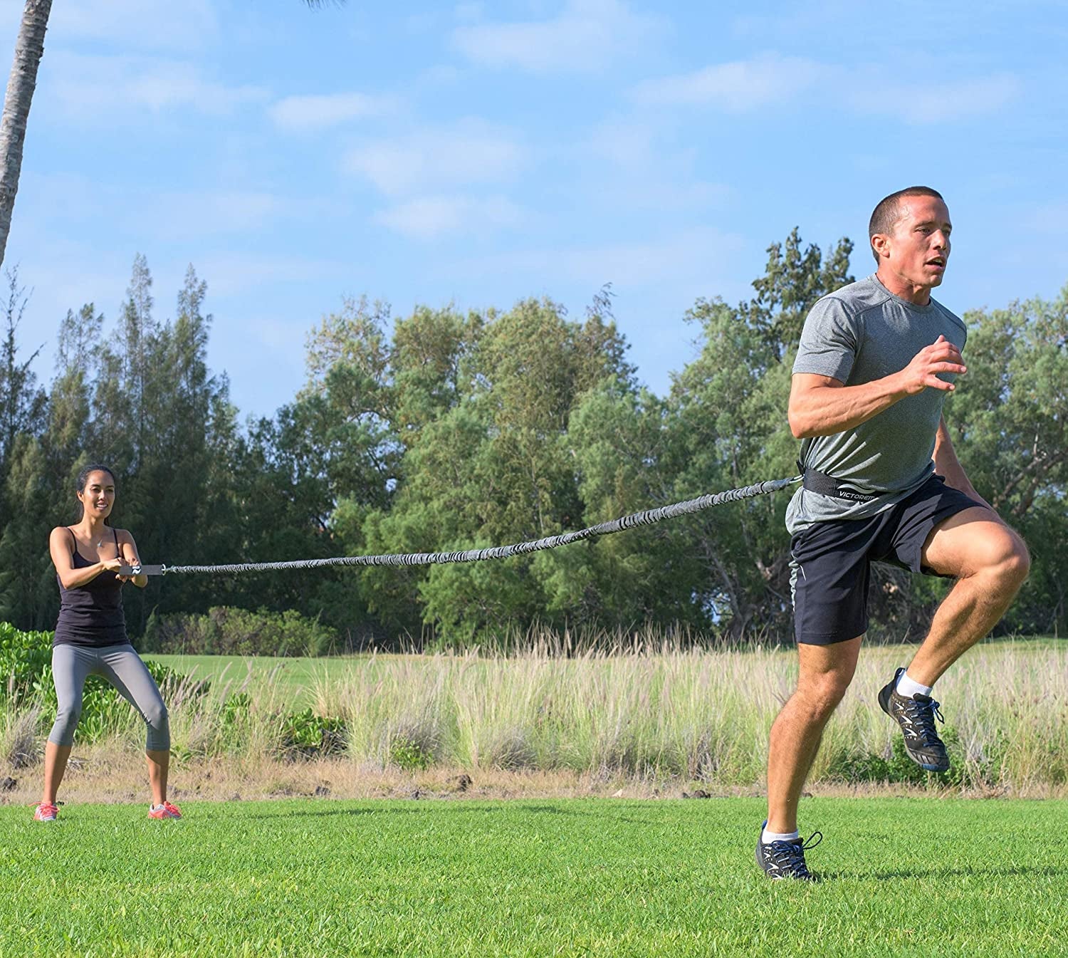 person holding bungee band while person runs forward with it attached to waist