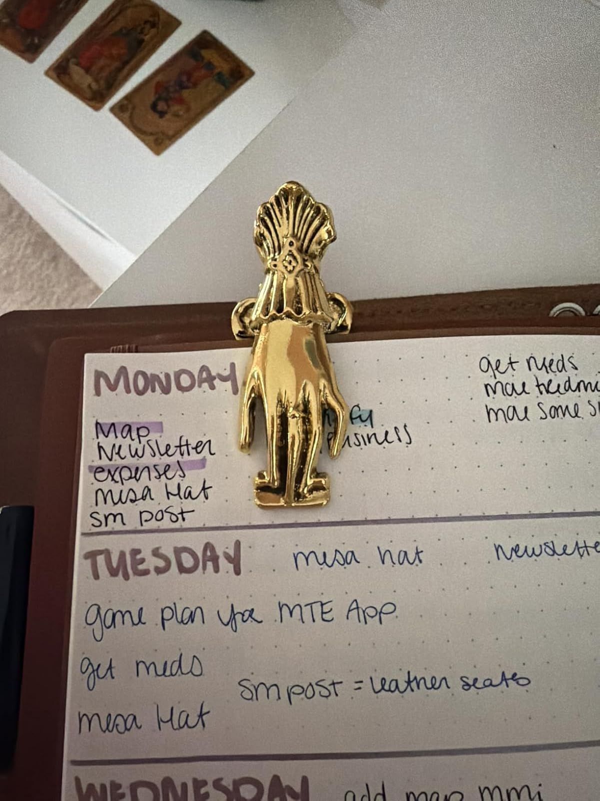 Gold hand-shaped clip holding a planner with handwritten weekly tasks, including meetings and newsletter tasks