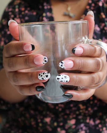 a reviewer holding a clear mug, showcasing a manicure with black and white design on nails