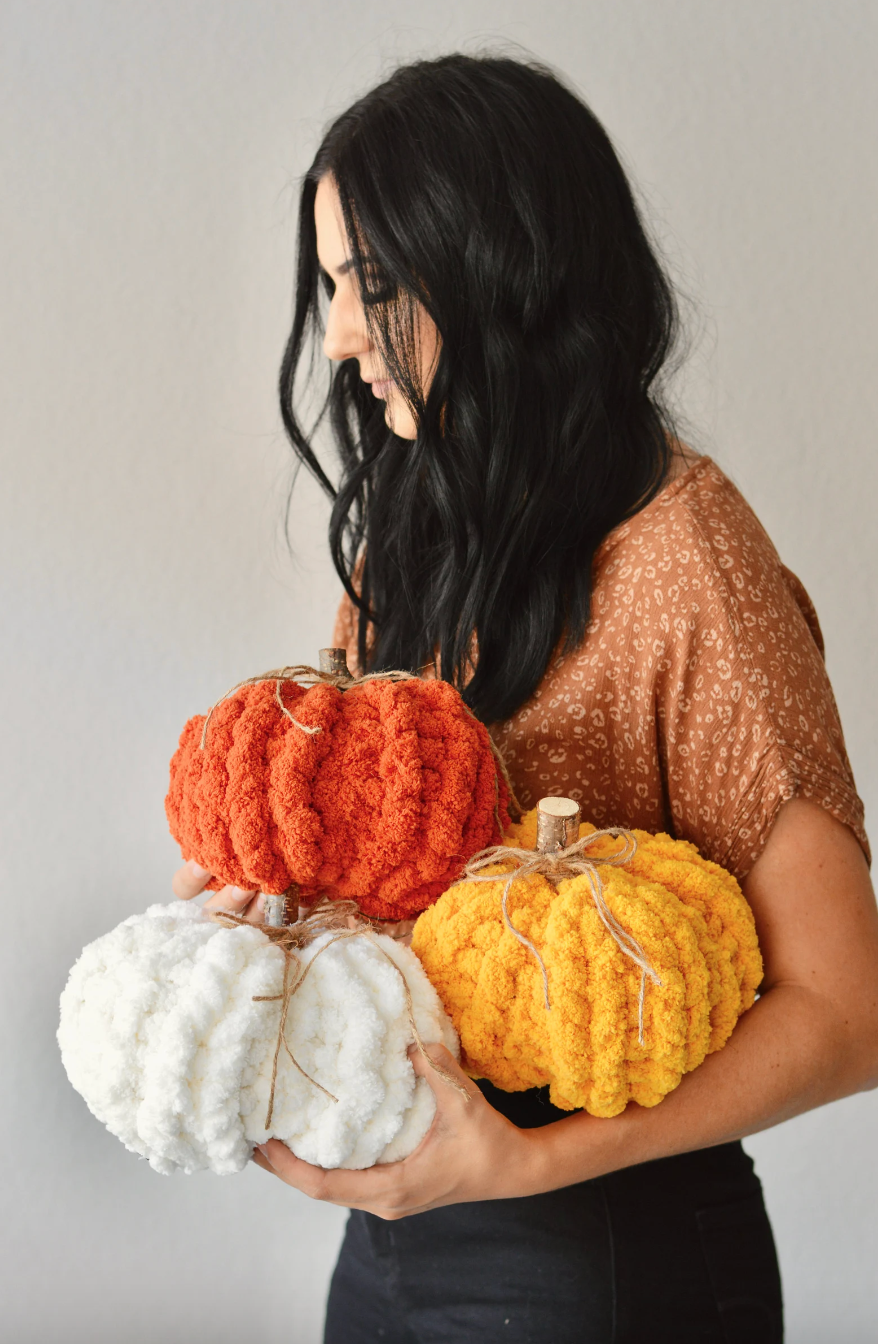 a model holding three knit pumpkins in orange, yellow, and white