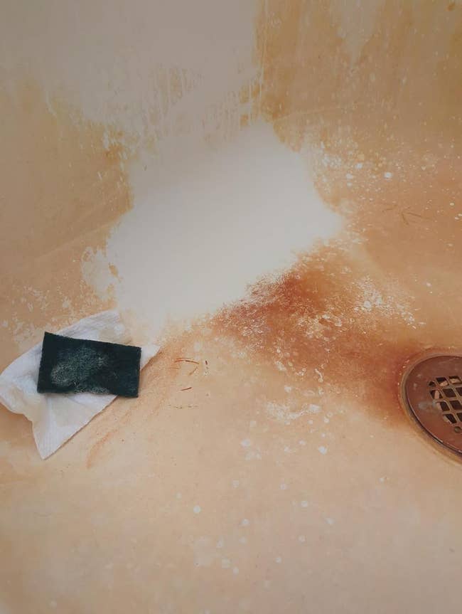Cleaning a bathtub with a sponge connected  a insubstantial  towel adjacent  to rust and soap residue adjacent   a drain