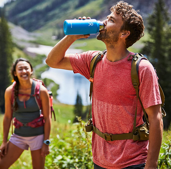 model drinking from the blue tumbler while backpacking while another model looks on