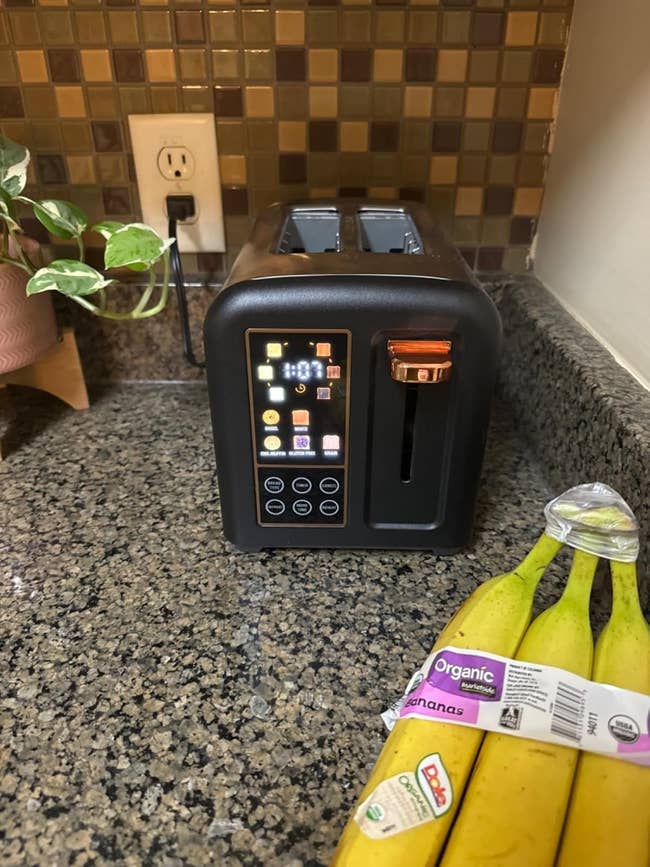 Smart toaster with digital display on a kitchen counter, next to a bunch of organic bananas