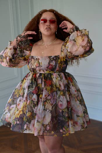 model in a floral patterned dress poses with hands in hair