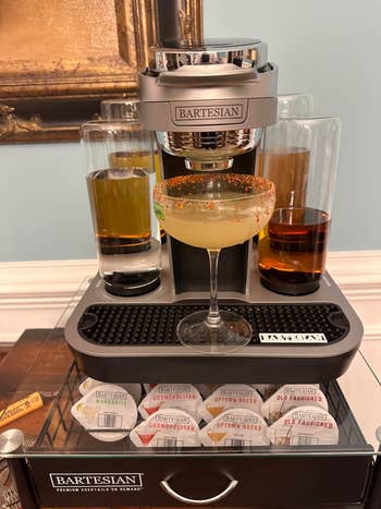 Bartesian premium cocktail machine with a margarita glass, surrounded by cocktail pod options, set on a wooden surface