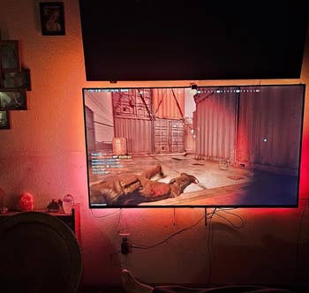 Gaming setup with a large screen displaying a game, ambient lighting, and a comfy seating area
