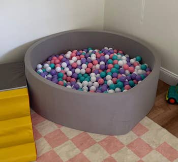 Entertainmment news An oval ball pit filled with multicolored balls is beside a yellow climbing structure on a pink checkered rug