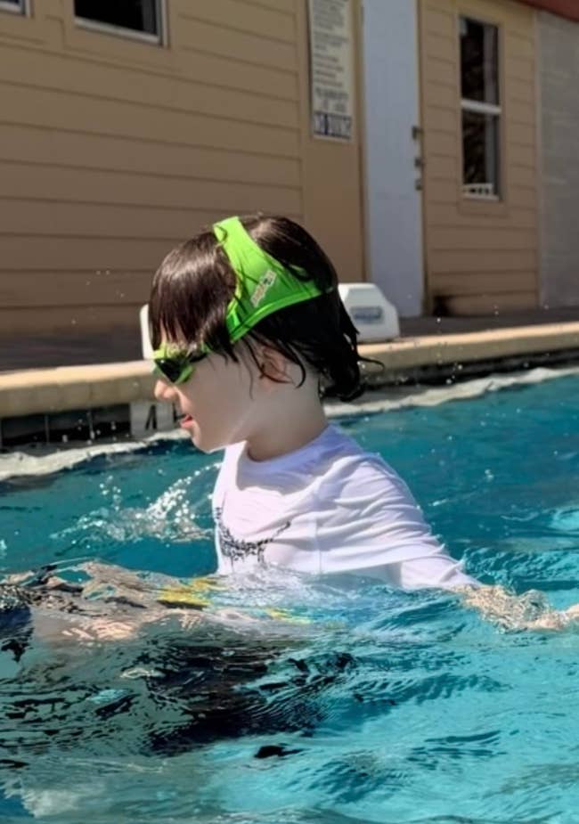 Child swimming successful a excavation with greenish goggles and achromatic shirt, focusing connected h2o activities