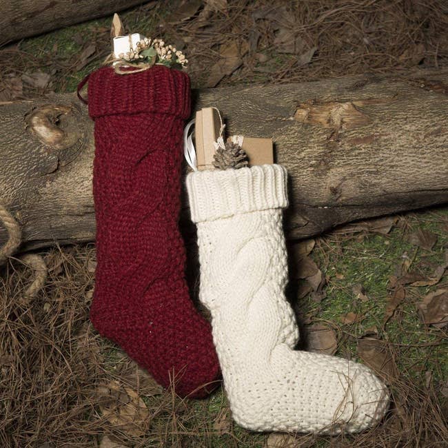 one red and one white christmas stocking on the ground outside, both filled with treats