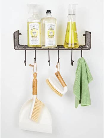 the white dustpan and brush hanging from a wall shelf filled with other cleaning supplies
