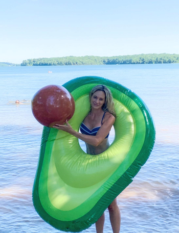 reviewer standing by a lake sticking their head through the hole in the green float and holding the ball