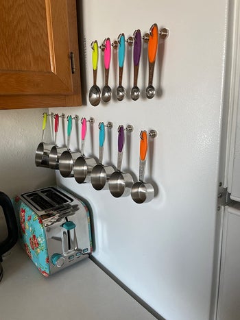 a reviewer using the hooks to hang measuring cups from the side of their fridge