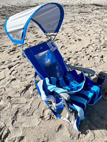 reviewer photo of their blue chair and sunshade with a striped towel draped on it