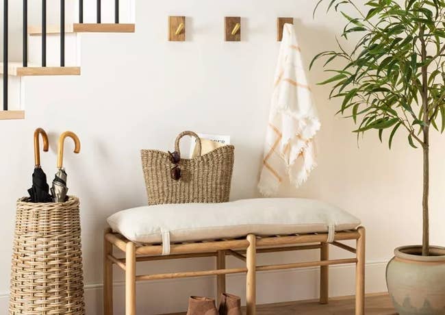 Wooden narrow natural bench with white plush cushion velcroed to it next to a floor plant and brown boots