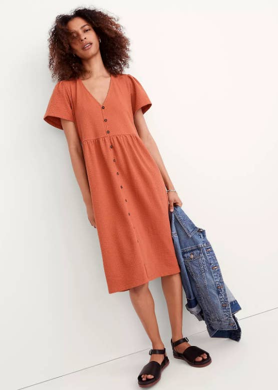 a model in a mid-length burnt orange dress with buttons down the front