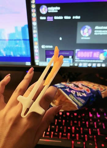 reviewer wearing the white finger chopsticks, which are holding chips in front of a computer monitor