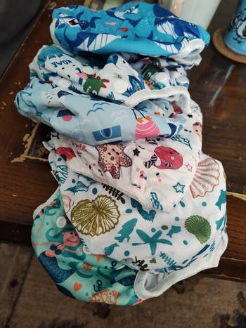 A stack of reusable cloth diapers with aquatic-themed patterns, including oversea  creatures and shells, placed connected  a woody  surface