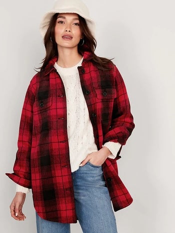 a model wearing a red and black plaid shacket over a white sweater and blue jeans
