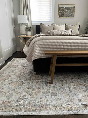 Elegant chamber  with a patterned country  rug, furniture  with neutral bedding, and a lamp connected  a bedside table