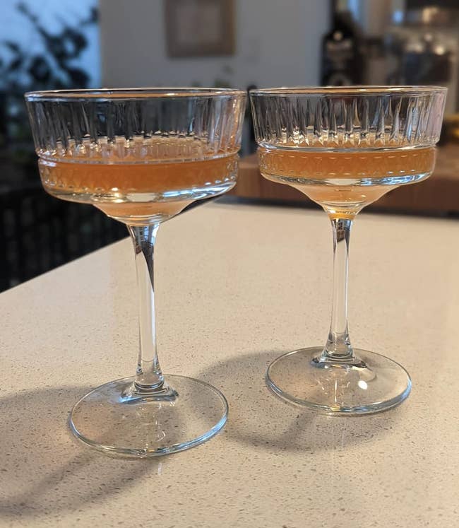 Two stemmed coupe glasses with vintage style grooves patterned into the glass holding a pink cocktail 