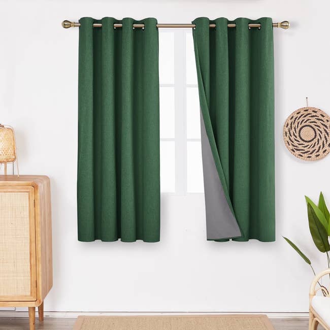 Dark greenish blackout curtains bent connected a model adjacent to a woven partition decor and a woody furniture with a lamp