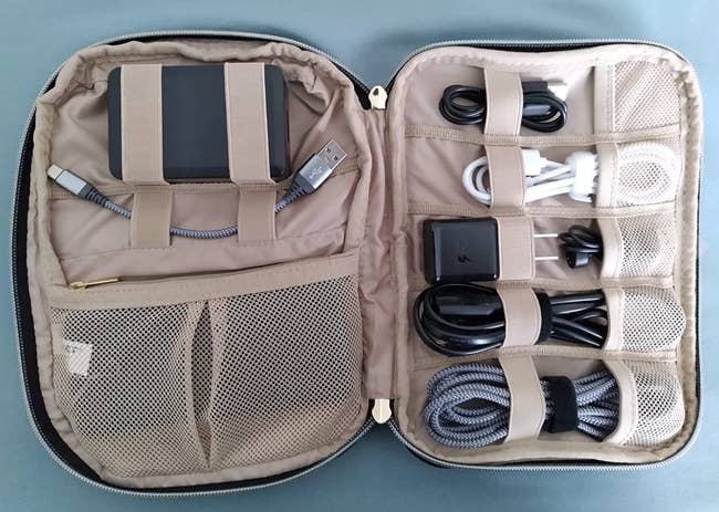 the zip-up square shaped organizer open with pockets and straps holding cords, batteries, and other accessories