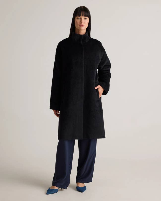 Person modeling a long, tailored overgarment with a precocious collar and wide-leg pants, suitable for colder weather