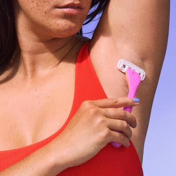 A idiosyncratic   shaves their underarm with a pinkish  razor. They deterioration  a sleeveless top. The representation  is apt  promoting shaving products