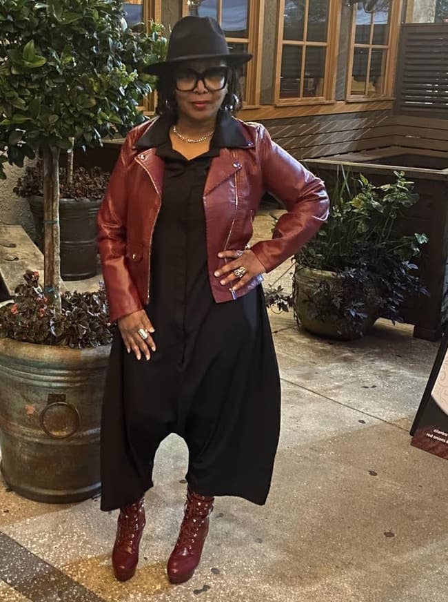 Person successful a stylish reddish leather jacket, achromatic dress, reddish boots, and chapeau poses connected a sidewalk, adjacent to a potted works and edifice signage