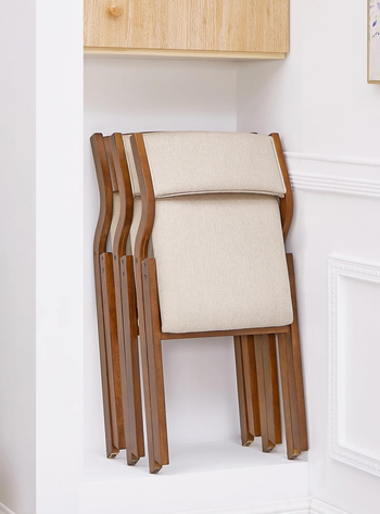 Beige folding chair with wooden frame, leaned against white wall under a shelf