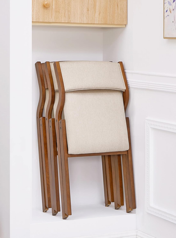 Beige folding chair with wooden frame, leaned against white wall under a shelf