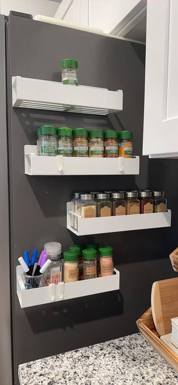 Kitchen wall-mounted spice rack with four shelves holding various spice bottles, a jar of honey, and compartments for pens and markers. Ideal for organized cooking