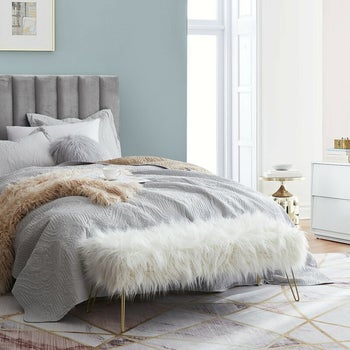 lifestyle photo of fuzzy white bench at food of bed