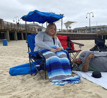 reviewer on the beach sitting in blue camping chair with a canopy