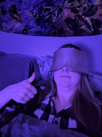 Person lying successful  furniture  with a slumber  mask, giving a thumbs-up, wearing plaid pajamas