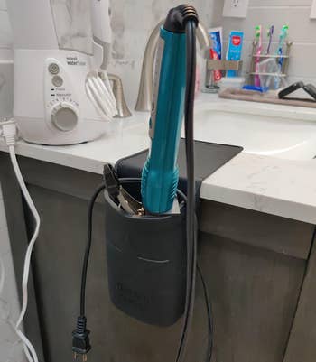 Hair styling tools stored in a black heat-resistant pouch hanging on a bathroom counter 