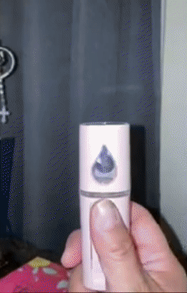 Reviewer pressing the button on the small pink device to let out a misting spray 