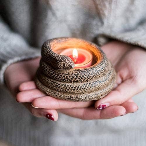 Person holding a candle holder shaped like a coiled snake with a lit candle