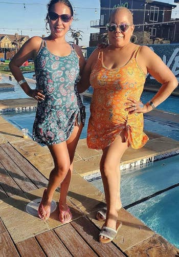 Two people in swimwear standing by a pool, one in a floral one-piece, the other in a printed tankini