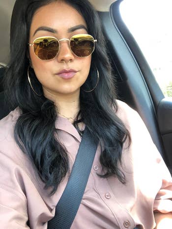 Person successful a car wearing sunglasses, hoop earrings, and a casual button-up shirt