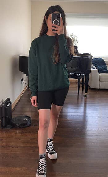 reviewer wearing the green crewneck with black bike shorts and sneakers